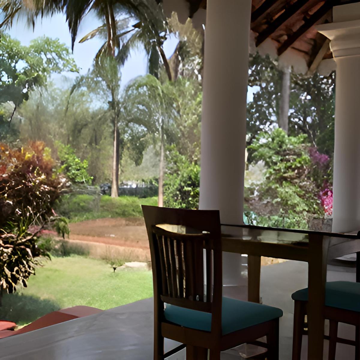 a table and chairs with a view of a yard at The Postcard Cuelim, Goa in Cansaulim