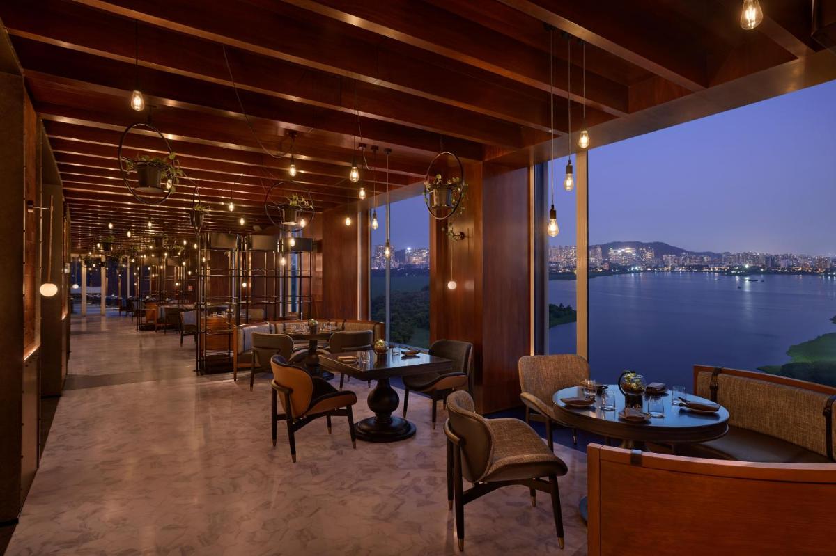 a restaurant with tables and chairs and a large window at The Westin Mumbai Powai Lake in Mumbai a restaurant with tables and chairs and a large window at The Westin Mumbai Powai Lake in Mumbai