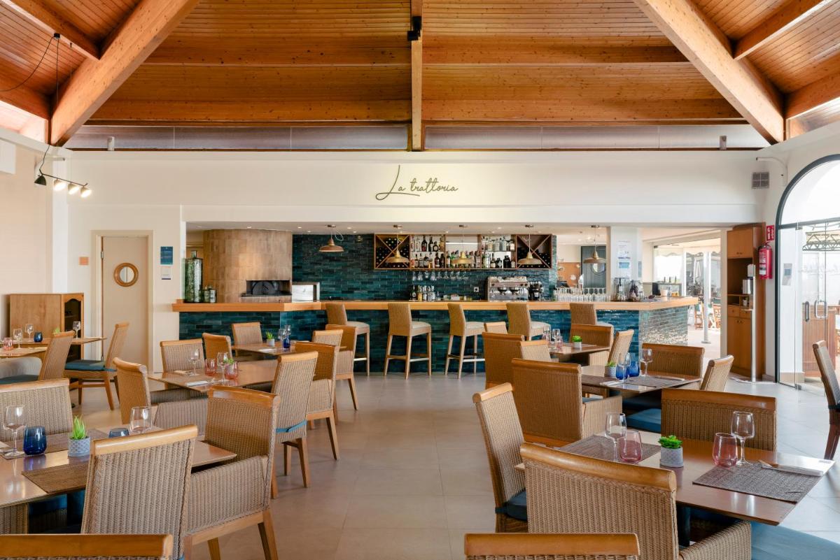 Un restaurante con techos de madera y mesas y sillas. en AluaSun Mediterráneo, en S'Algar