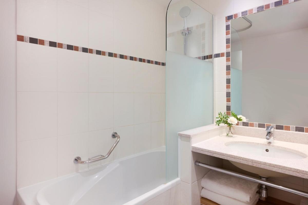 une salle de bain blanche avec une baignoire et un lavabo dans l'établissement Fraser Suites Paris La Défense, à Courbevoie