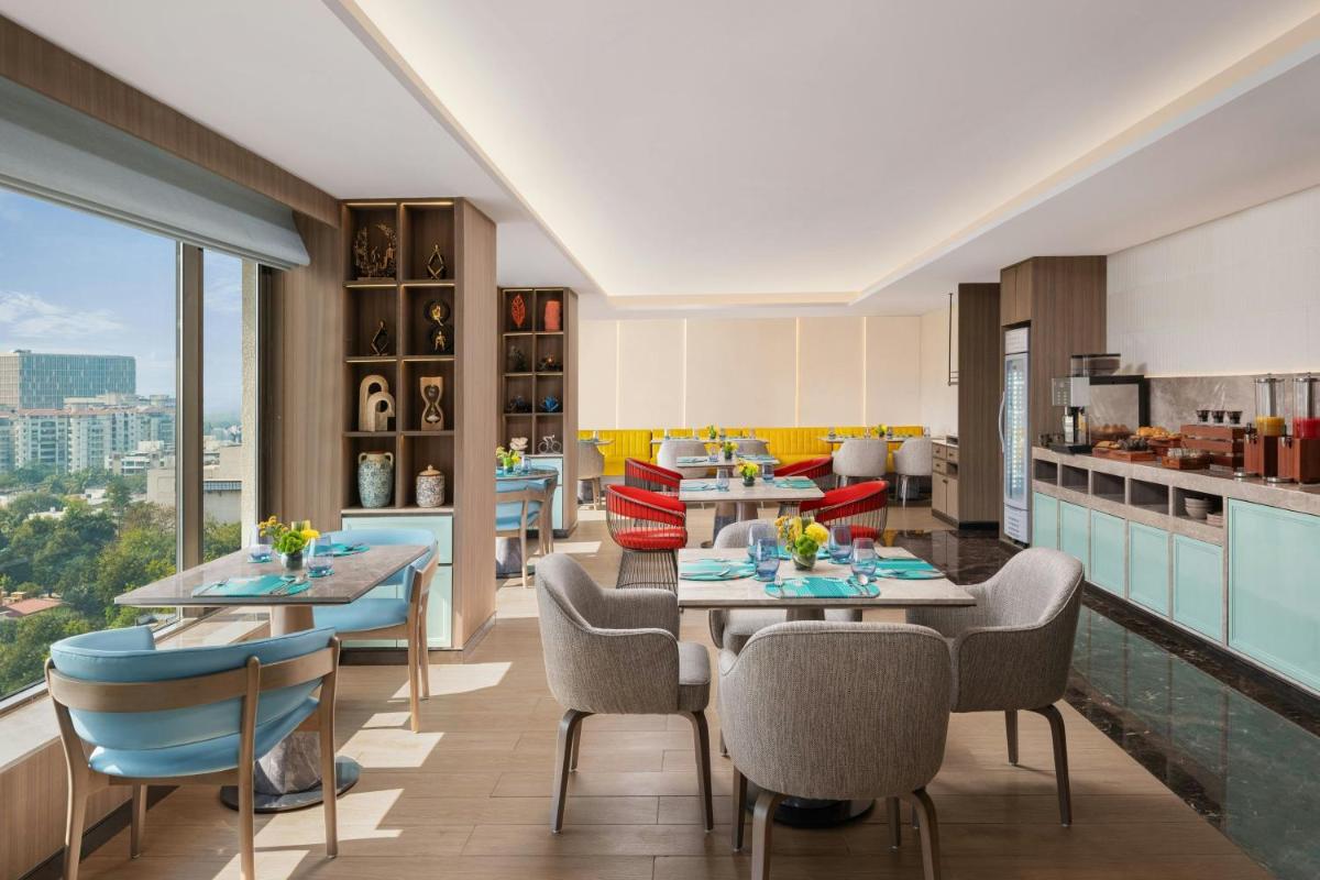 a dining room with tables and chairs and a kitchen at Le Meridien Ahmedabad in Ahmedabad