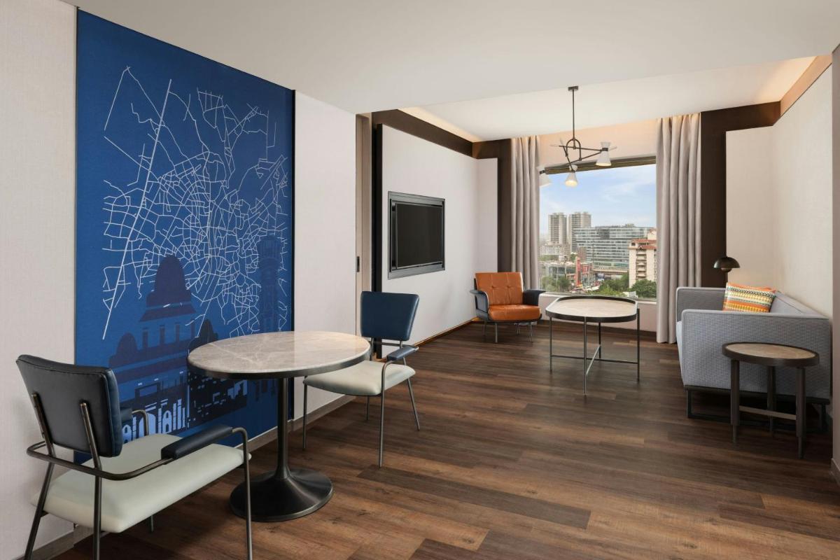 a living room with tables and chairs and a tv at Le Meridien Ahmedabad in Ahmedabad
