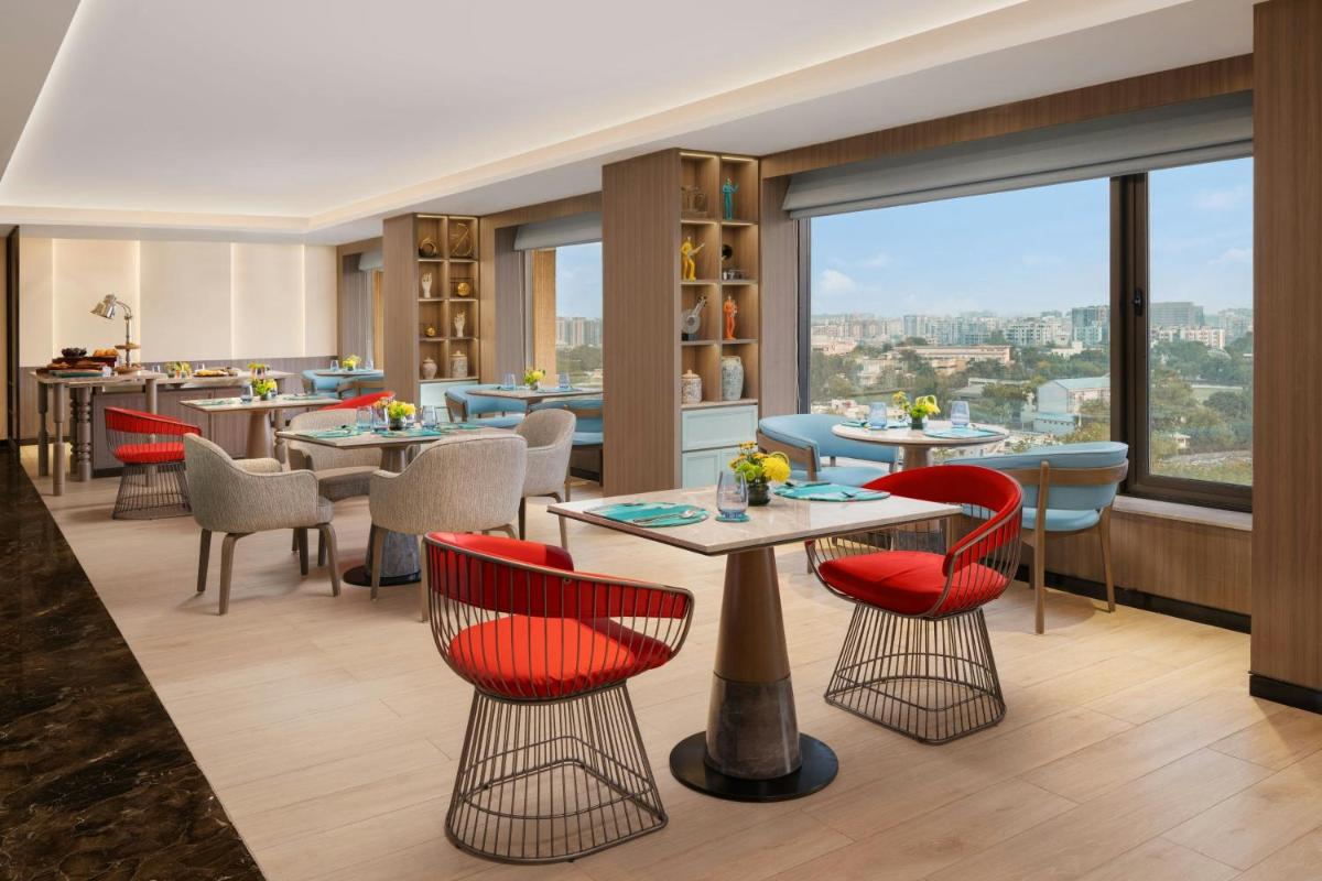 a restaurant with tables and chairs and a large window at Le Meridien Ahmedabad in Ahmedabad