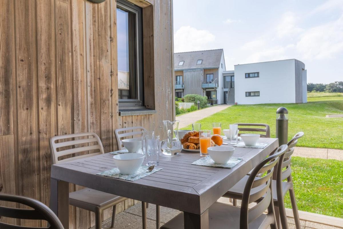 une table en bois avec des chaises et une table d'extérieur avec du jus d'orange dans l'établissement Résidence Odalys Fleur de Sel, à Guidel-Plage