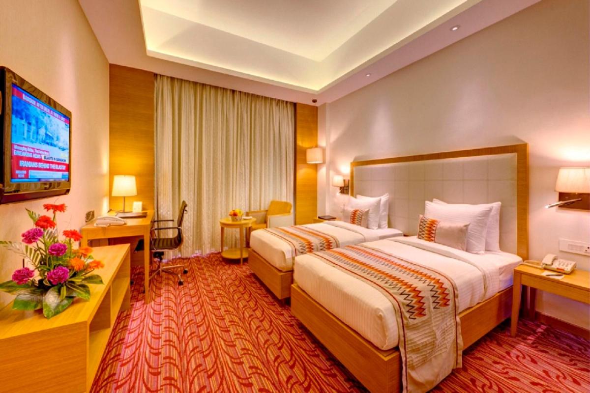 a hotel room with two beds and a television at Pride Plaza Hotel, Kolkata in Kolkata