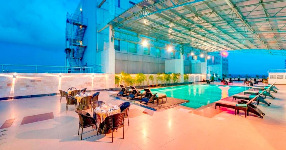 a pool with tables and chairs next to a building at Pride Plaza Hotel, Kolkata in Kolkata