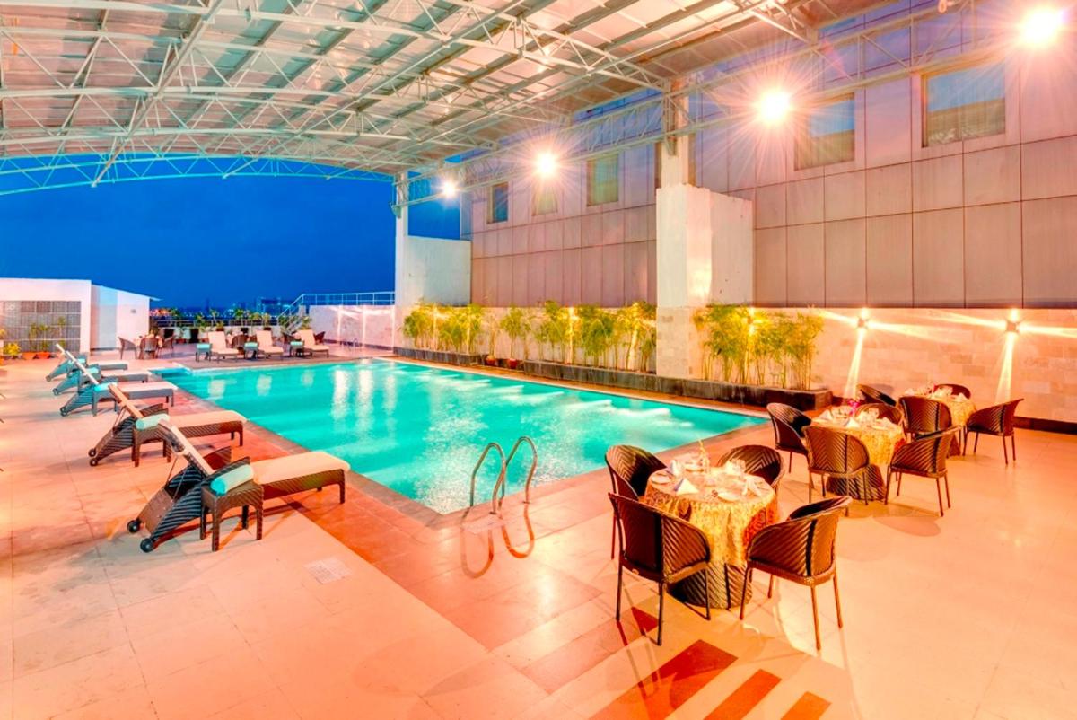 a pool with tables and chairs next to a building at Pride Plaza Hotel, Kolkata in Kolkata