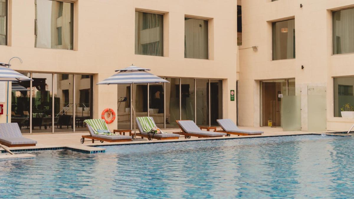 a pool with chairs and umbrellas next to a building at Holiday Inn New Delhi Aerocity by IHG in New Delhi