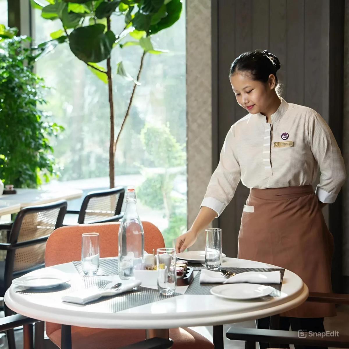 a woman is setting a table in a restaurant at The Residency Towers in Chennai