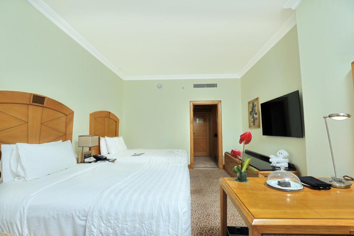 a bedroom with a bed and a desk and a tv at Le Royal Meridien Chennai in Chennai