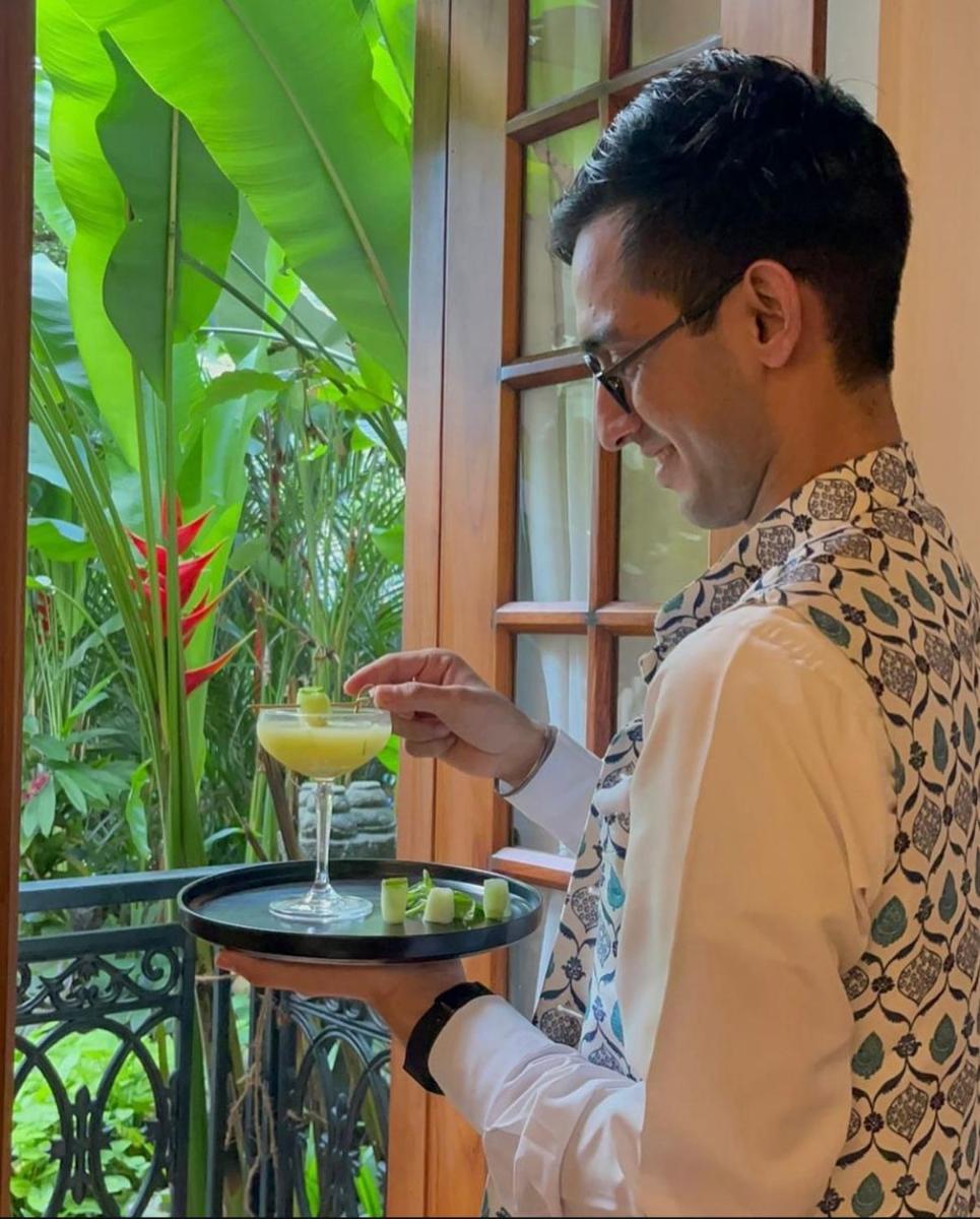 a man is holding a drink on a table at The Postcard Saligao in Calangute