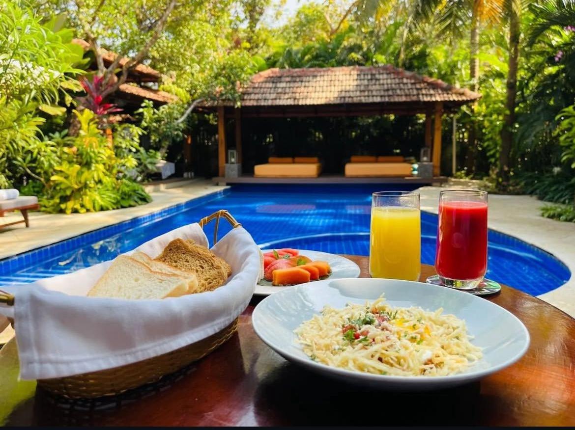 a table topped with plates of food and drinks next to a pool at The Postcard Saligao in Calangute
