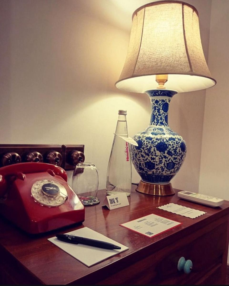 a table with a lamp and a telephone on it at The Postcard Saligao in Calangute
