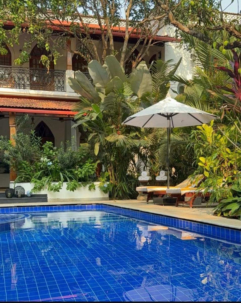 a pool in front of a house with an umbrella at The Postcard Saligao in Calangute