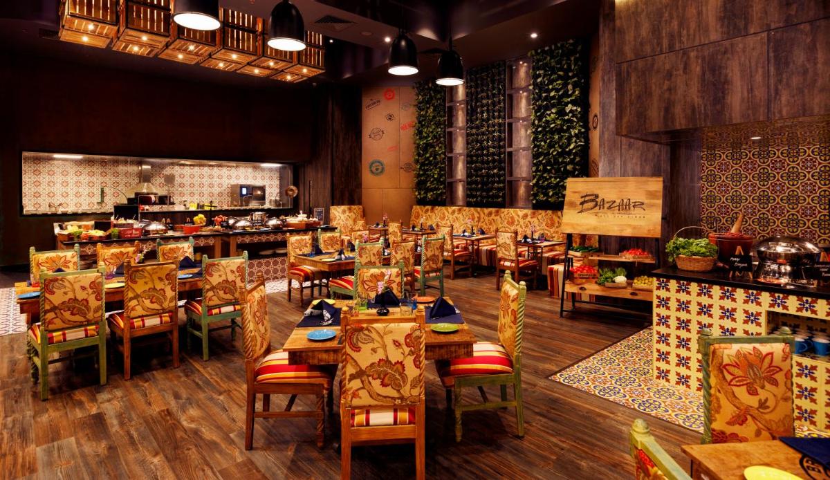 a restaurant with wooden tables and chairs and a kitchen at Grand Chennai by GRT Hotels in Chennai