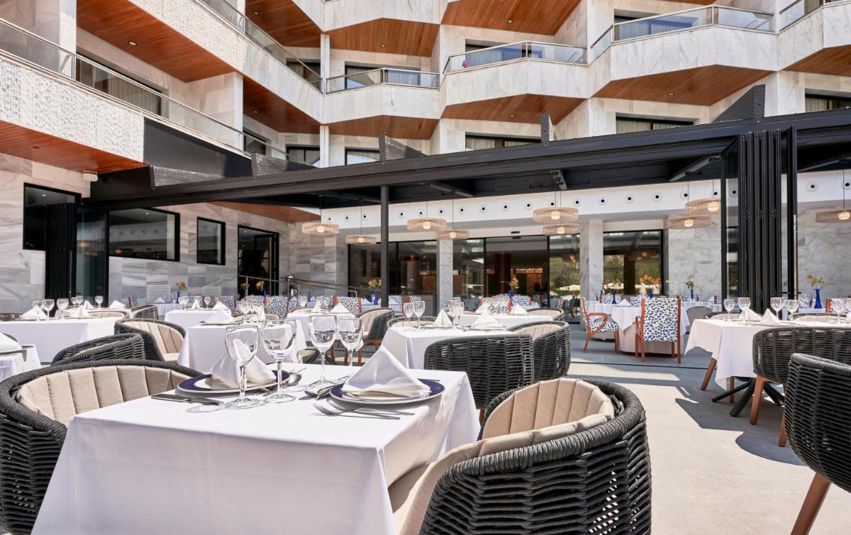 Un restaurante con mesas y sillas blancas y un edificio. en Hotel Serrano Palace, en Cala Ratjada