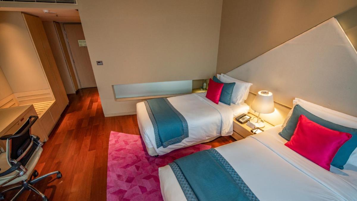 a hotel room with two beds with red and blue pillows at Vivanta New Delhi, Dwarka in New Delhi a hotel room with two beds with red and blue pillows at Vivanta New Delhi, Dwarka in New Delhi