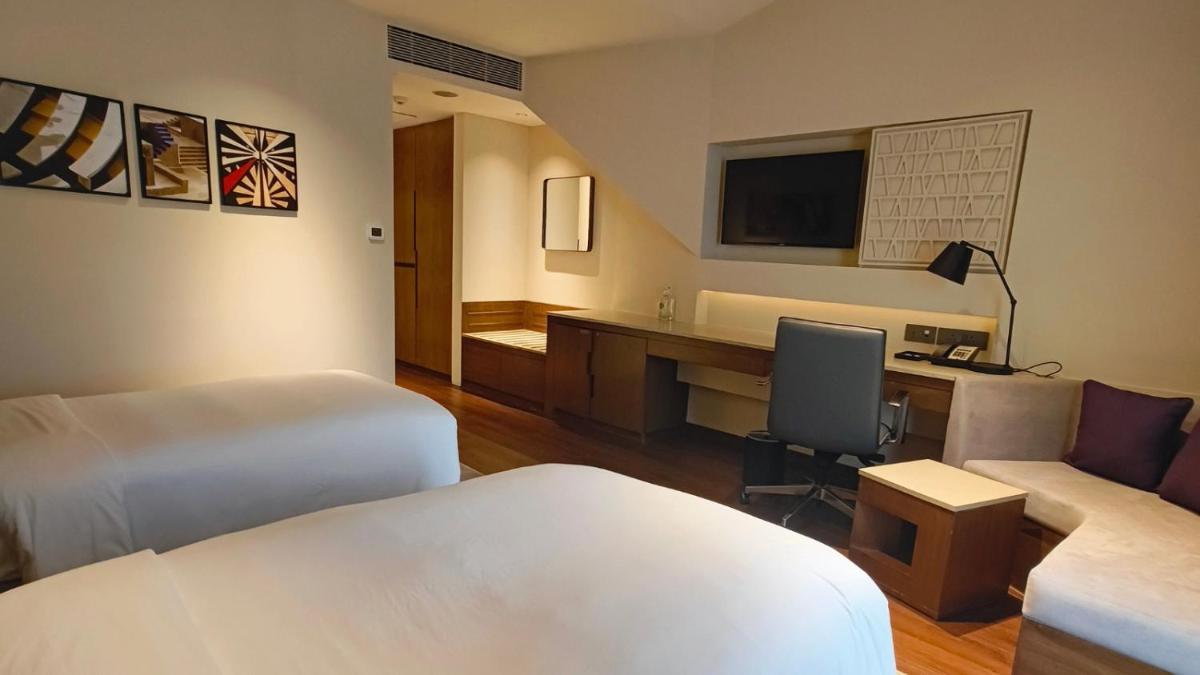 a hotel room with two beds and a desk at Vivanta New Delhi, Dwarka in New Delhi a hotel room with two beds and a desk at Vivanta New Delhi, Dwarka in New Delhi