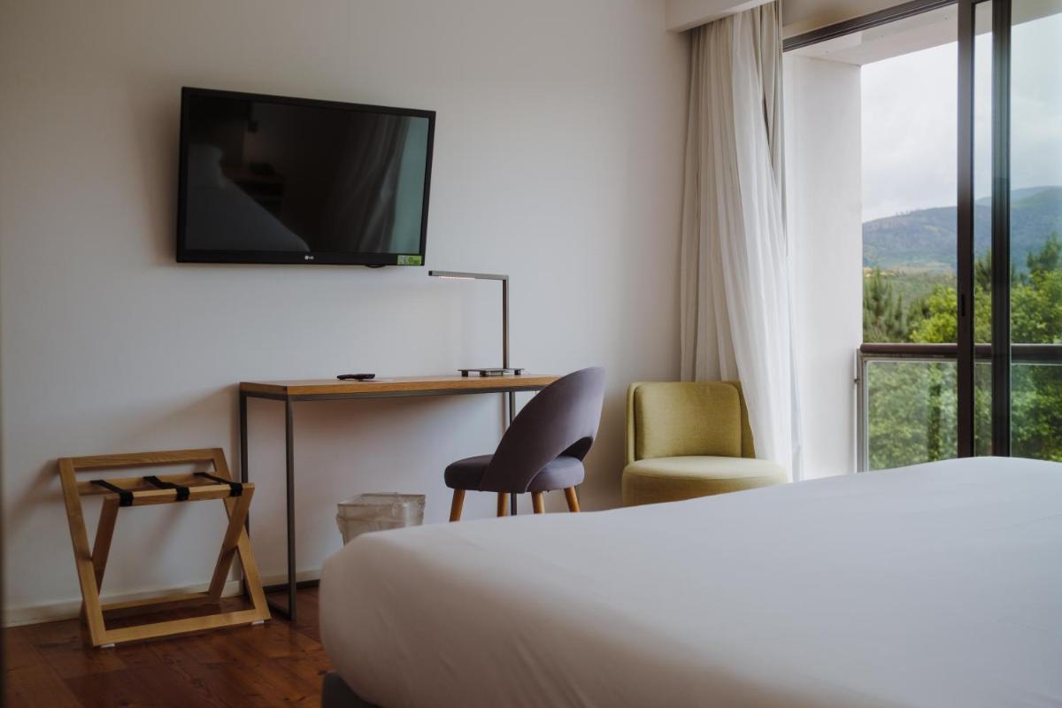 um quarto de hotel com cama, TV e cadeira em Monte Prado Hotel & Spa em Melgaço