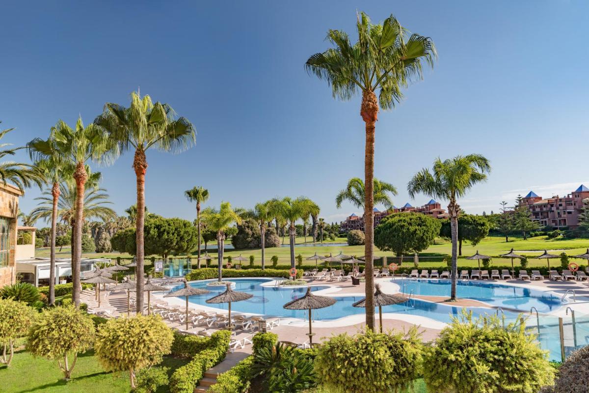 Una vista de una piscina con palmeras y sombrillas. en Elba Costa Ballena Beach & Thalasso Resort, en Costa Ballena