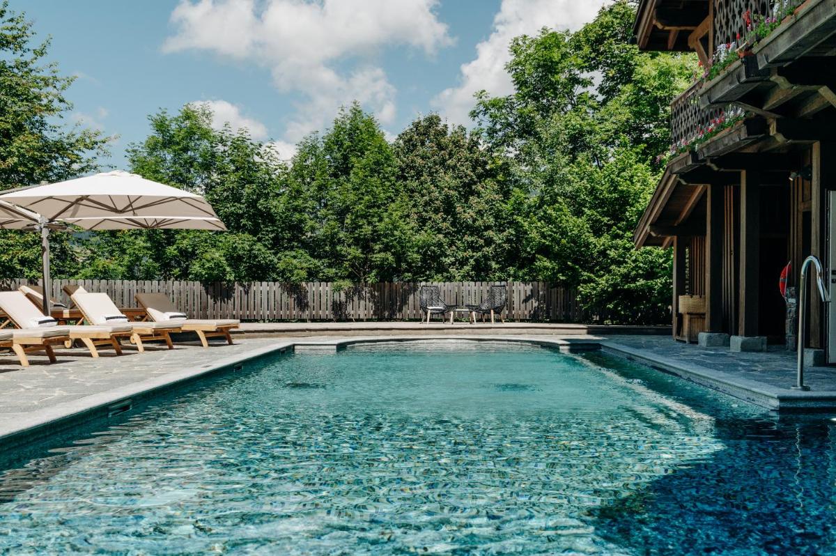 une piscine avec des chaises et un parasol dans l'établissement Les Chalets du Mont d'Arbois & Spa, Megève, à Megève une piscine avec des chaises et un parasol dans l'établissement Les Chalets du Mont d'Arbois & Spa, Megève, à Megève
