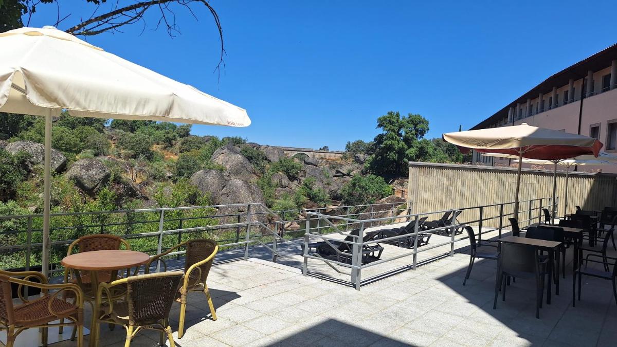 Un patio con sillas, mesas y sombrillas. en Hotel Balneario de Retortillo, en Retortillo