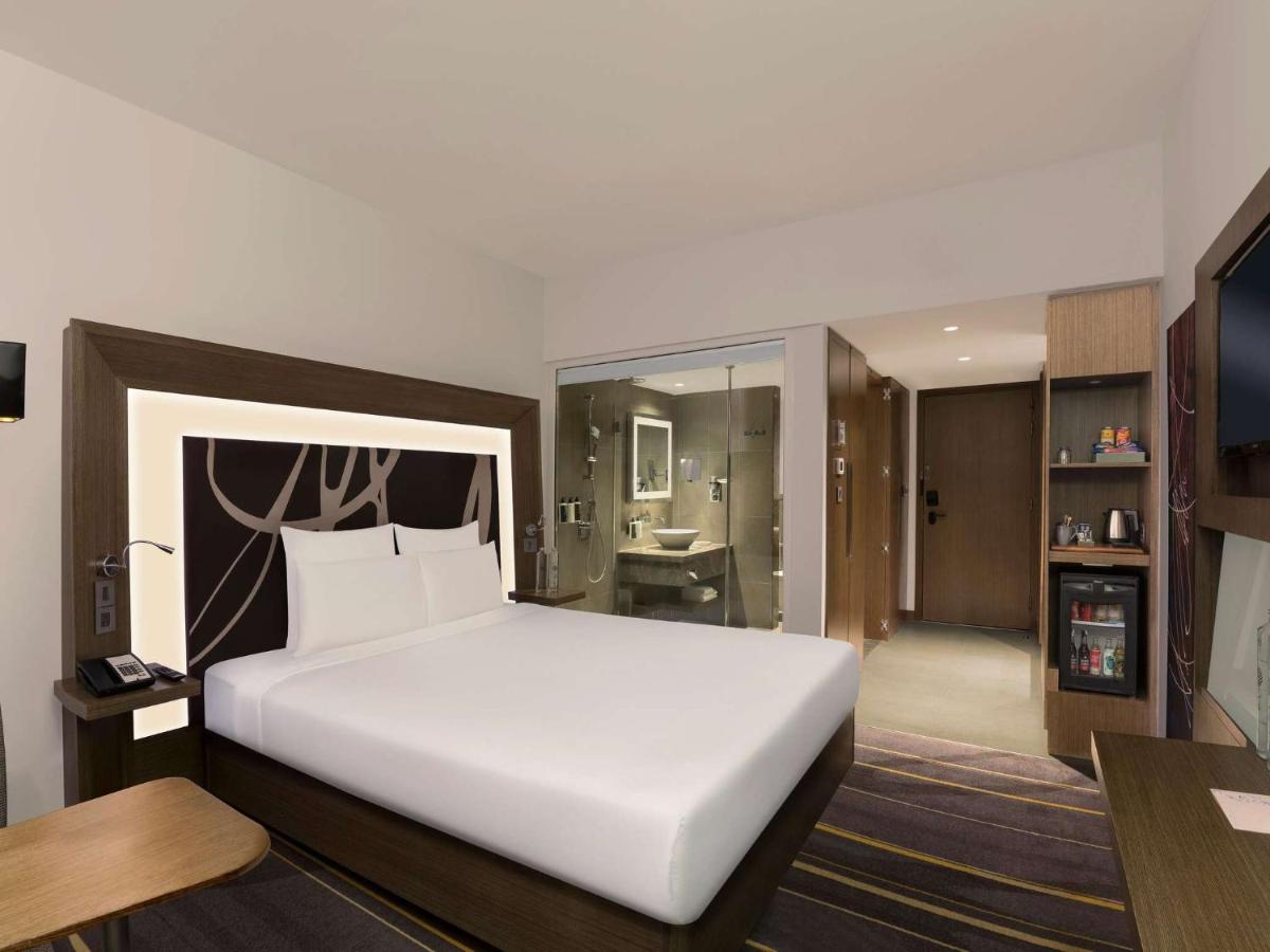 a bedroom with a large white bed and a bathroom at Novotel New Delhi Aerocity in New Delhi