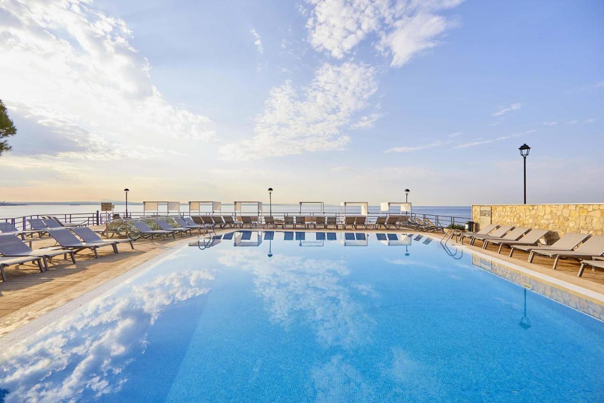 Una gran piscina con sillas y el océano. en Barceló Illetas Albatros - Adults Only, en Illetas