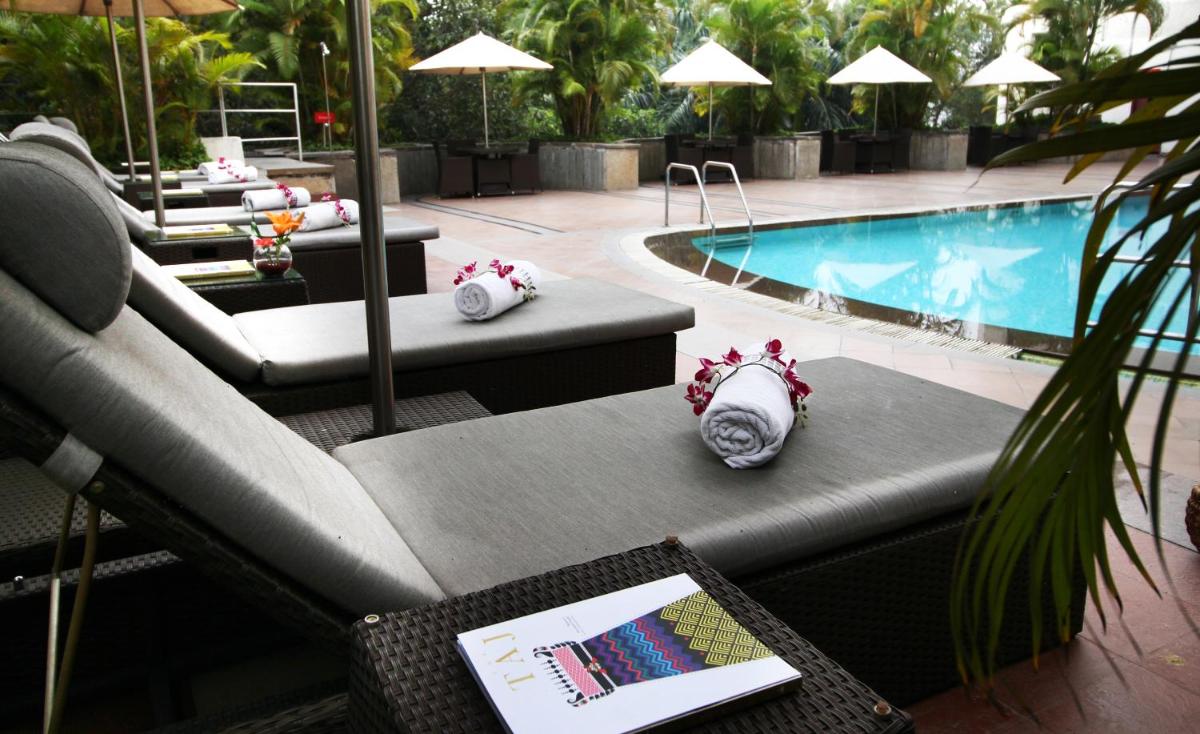 a swimming pool with couches and a table with a book at Vivanta Bengaluru Residency Road in Bengaluru a swimming pool with couches and a table with a book at Vivanta Bengaluru Residency Road in Bengaluru
