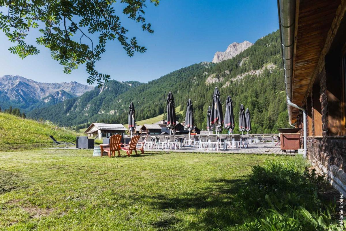 un groupe de tables et de chaises avec des parasols et des montagnes dans l'établissement Hotel Spa L'Equipe, à Molines-en-Queyras