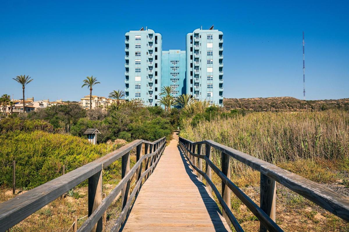 un puente de madera con edificios altos en el fondo en Hotel Playas de Guardamar, en Guardamar del Segura