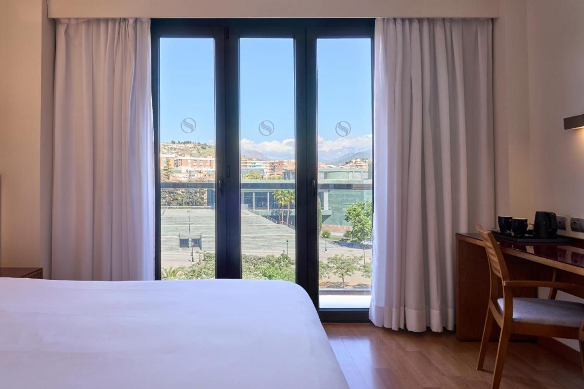 Un dormitorio con una cama, un escritorio y ventanas. en Senator Granada, en Granada