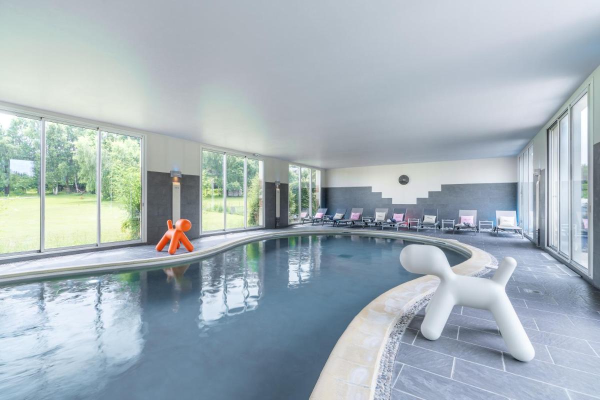 une piscine avec deux personnes dans un bâtiment dans l'établissement Le Manoir De La Poterie & Spa, à Cricquebœuf