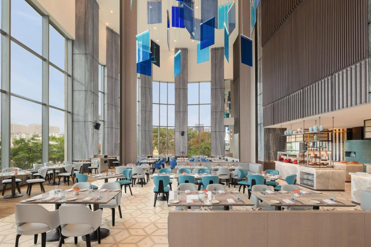 a restaurant with tables and chairs and large windows at Le Meridien Ahmedabad in Ahmedabad