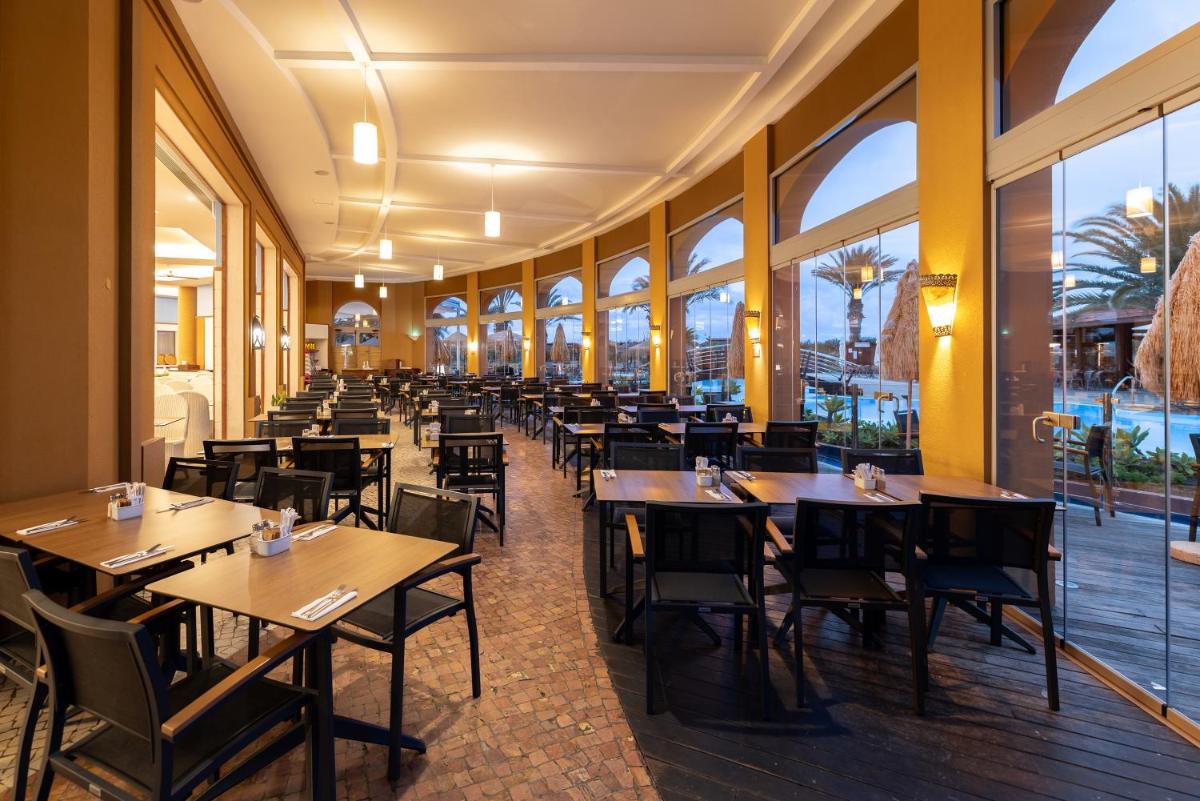 um restaurante com mesas e cadeiras e grandes janelas em Pestana Porto Santo Premium All Inclusive Beach & SPA Resort em Porto Santo