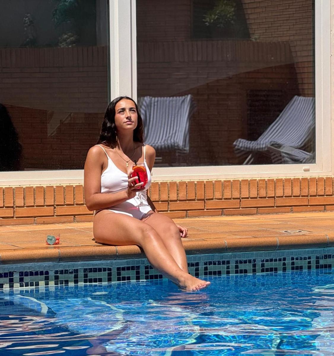 Una mujer en traje de baño sentada junto a una piscina. en Aparthotel Los Girasoles, en Zaragoza