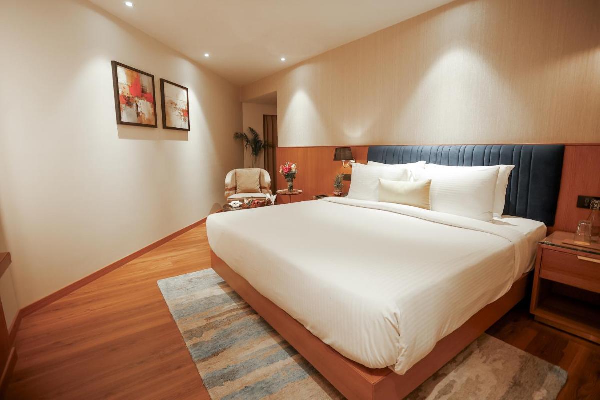 a bedroom with a large white bed and a chair at Golden Tulip Jaipur in Jaipur