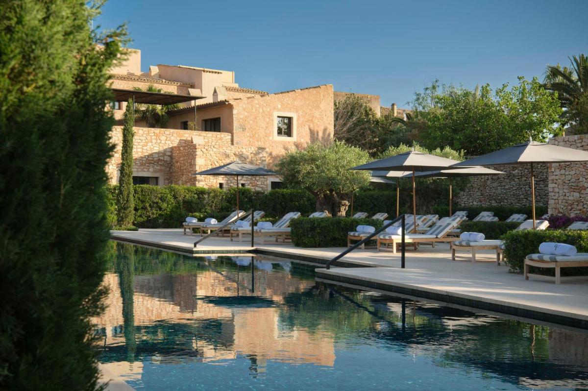 Una piscina con sillas y sombrillas al lado de un edificio. en Can Ferrereta, en Santanyí