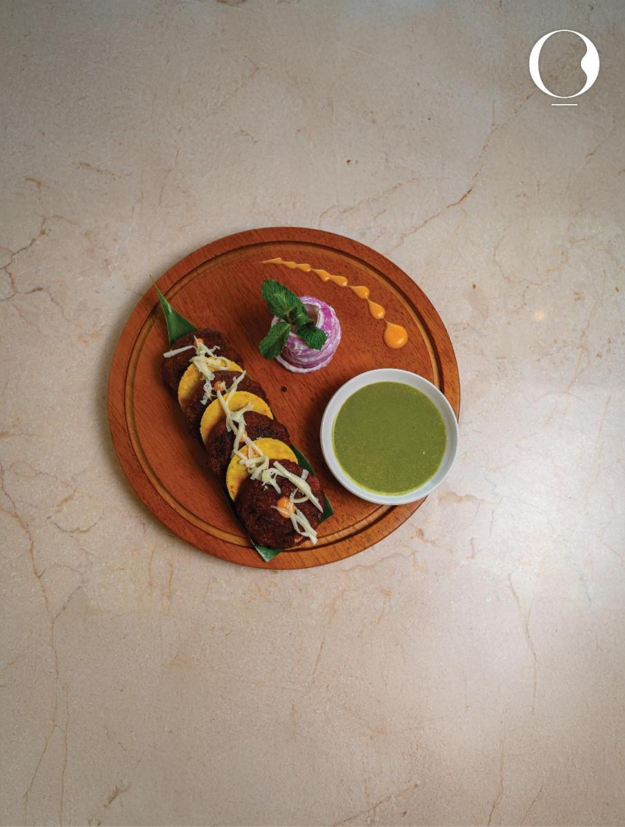 a plate with a hot dog and a bowl of green sauce at Miros - Formerly Imperial Goa in Old Goa