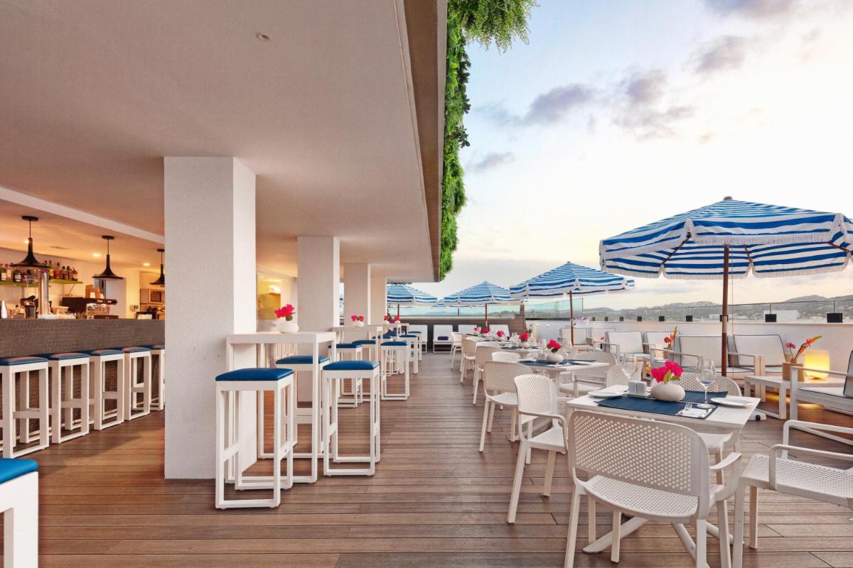 un restaurante con sillas blancas, mesas y sombrillas en Eurostars Puerto de Ibiza, en Ibiza