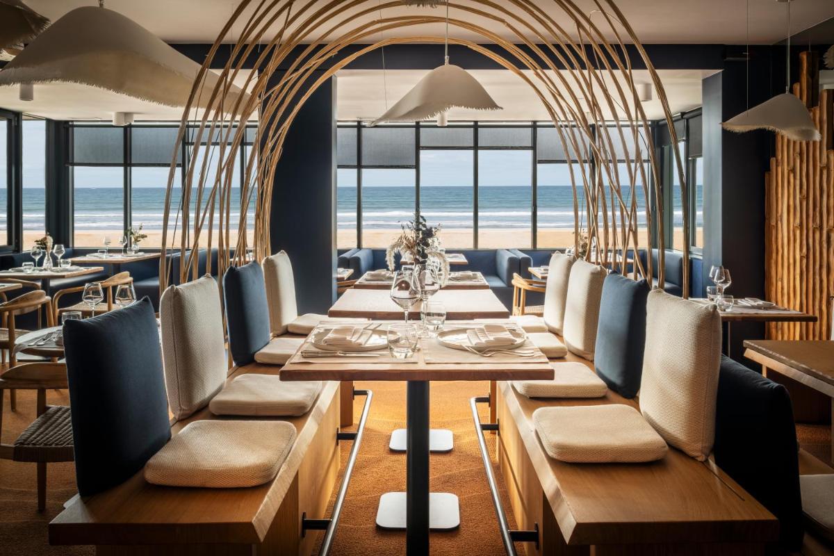 un restaurant avec une table et des chaises avec la plage en arrière-plan dans l'établissement Atlantic Hôtel & Spa, à Les Sables-dʼOlonne