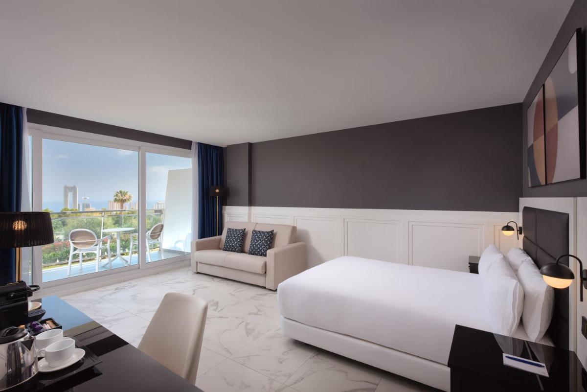 Un dormitorio con una cama blanca y una habitación con balcón. en Four Points by Sheraton Costa Blanca Resort, en Benidorm