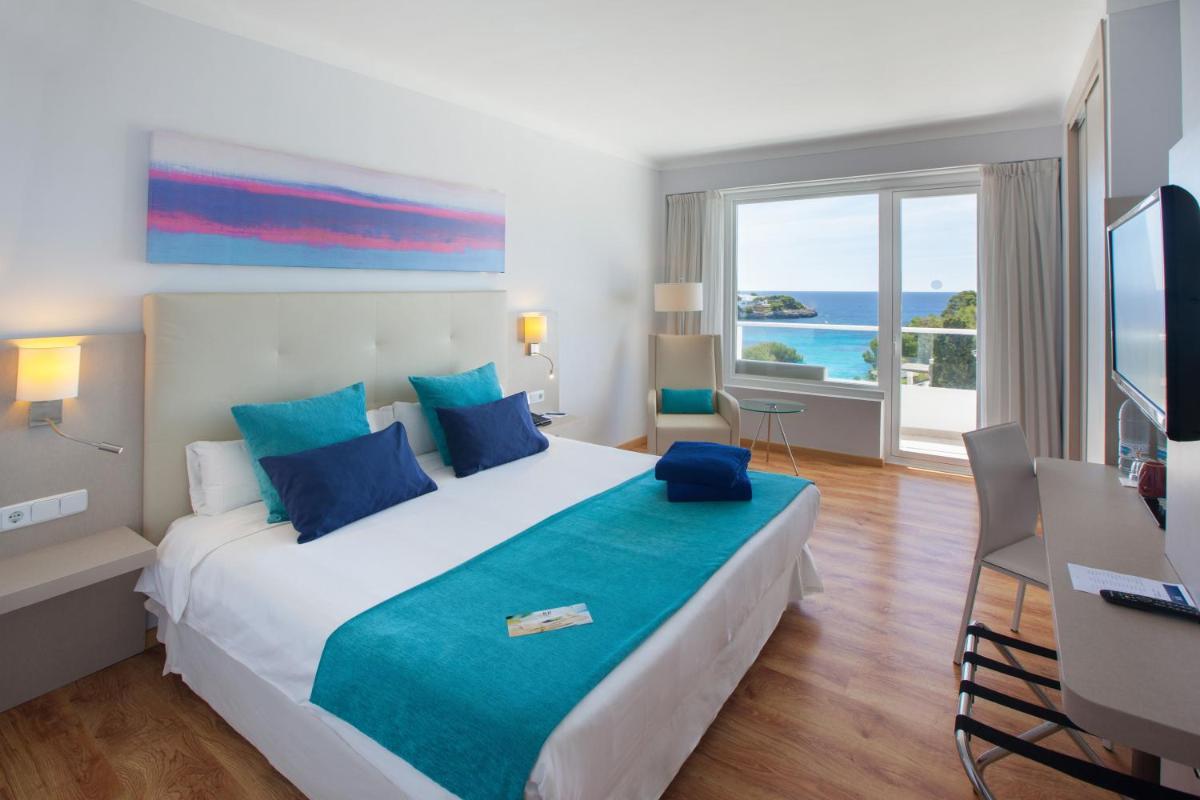Una habitación de hotel con una cama, un escritorio y una ventana. en Grupotel Rocador - Adults Only, en Cala d´Or