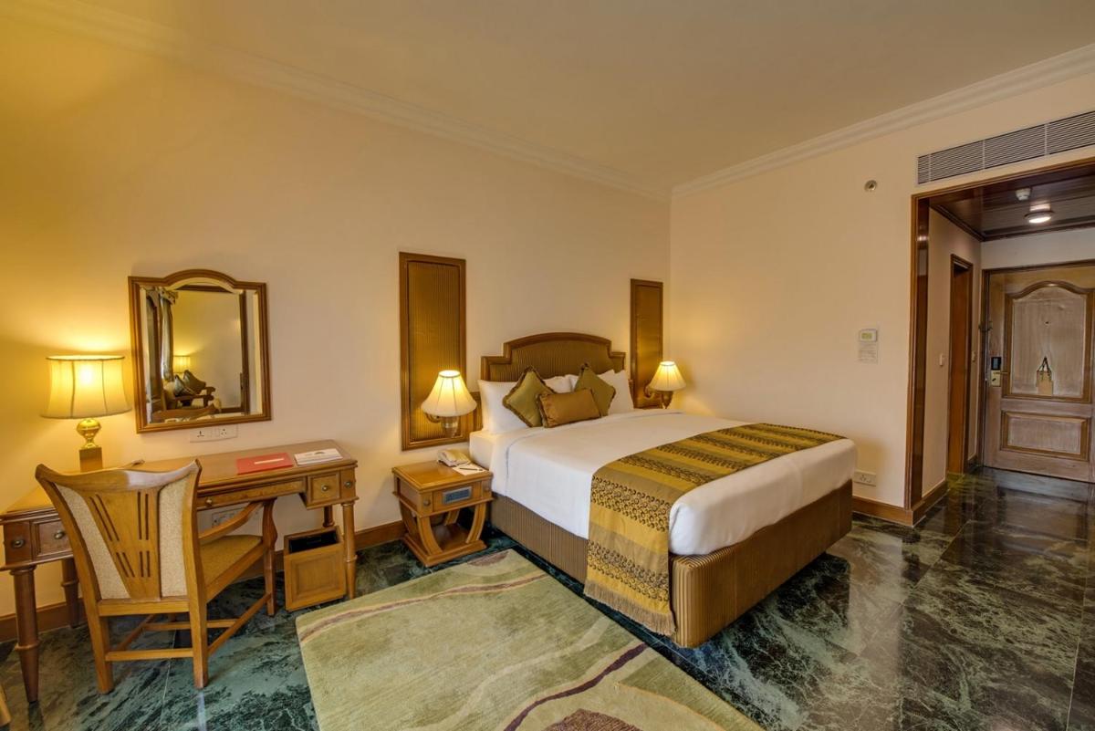 a hotel room with a bed and a desk and a mirror at The Ummed Ahmedabad Airport in Ahmedabad
