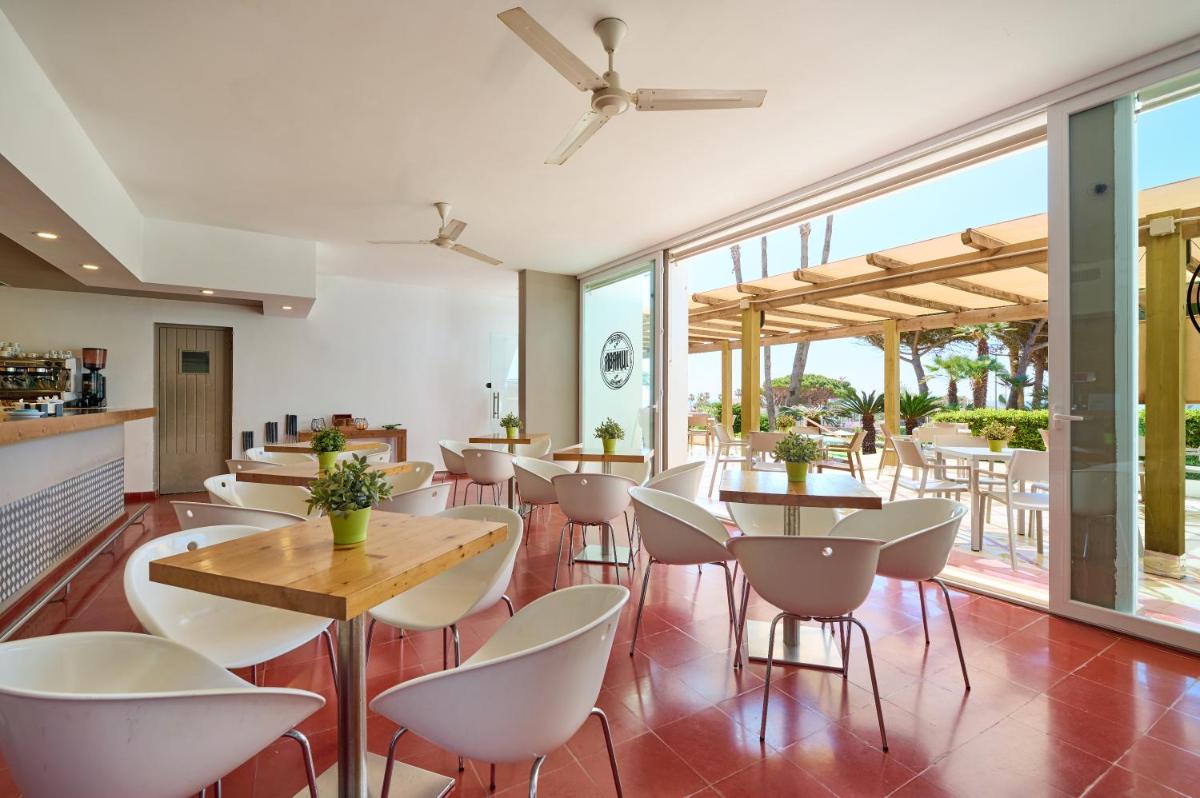 Un restaurante con sillas y mesas blancas y ventanas. en Alua Illa de Menorca, en S'Algar