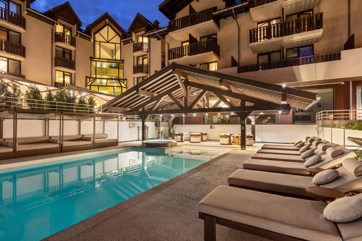 une piscine avec des chaises longues à côté d'un bâtiment dans l'établissement Hôtel Les Aiglons Chamonix, à Chamonix-Mont-Blanc