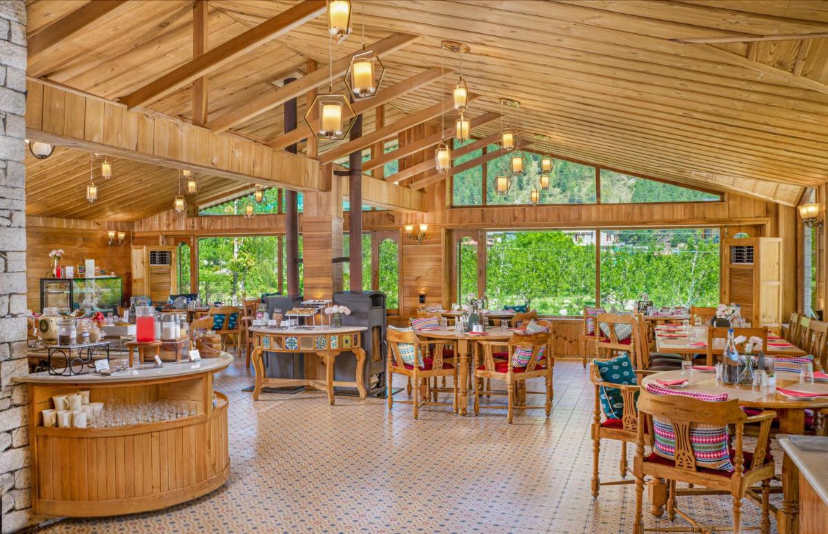a restaurant with wooden floors and tables and chairs at Storii By ITC Hotels Urvashis Retreat, Manali in Manāli a restaurant with wooden floors and tables and chairs at Storii By ITC Hotels Urvashis Retreat, Manali in Manāli