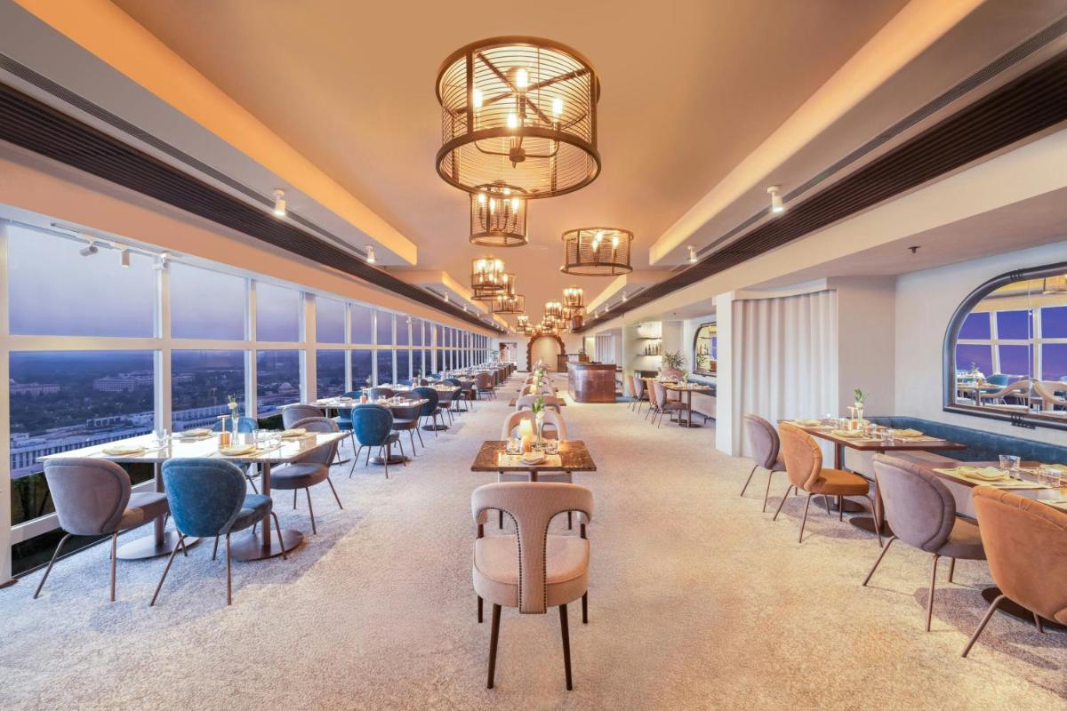 a restaurant with tables and chairs and windows at Le Meridien New Delhi in New Delhi a restaurant with tables and chairs and windows at Le Meridien New Delhi in New Delhi