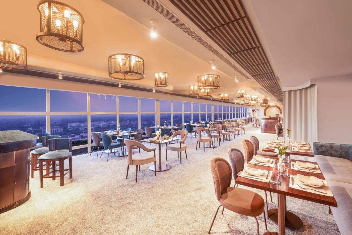 a restaurant with tables and chairs and large windows at Le Meridien New Delhi in New Delhi a restaurant with tables and chairs and large windows at Le Meridien New Delhi in New Delhi