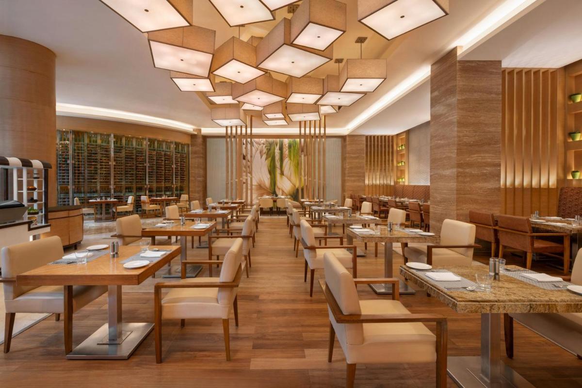 a restaurant with wooden tables and chairs and a large chandelier at Bengaluru Marriott Hotel Whitefield in Bengaluru